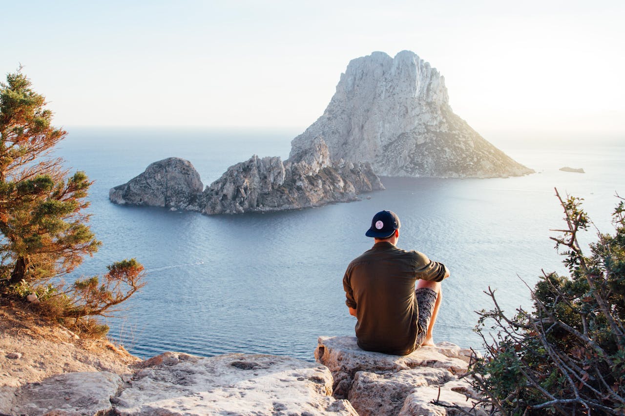 Contact Man enjoys a scenic view of Es VedrĂ at sunset from a cliff in San Juan Bautista, providing a perfect summer escape.